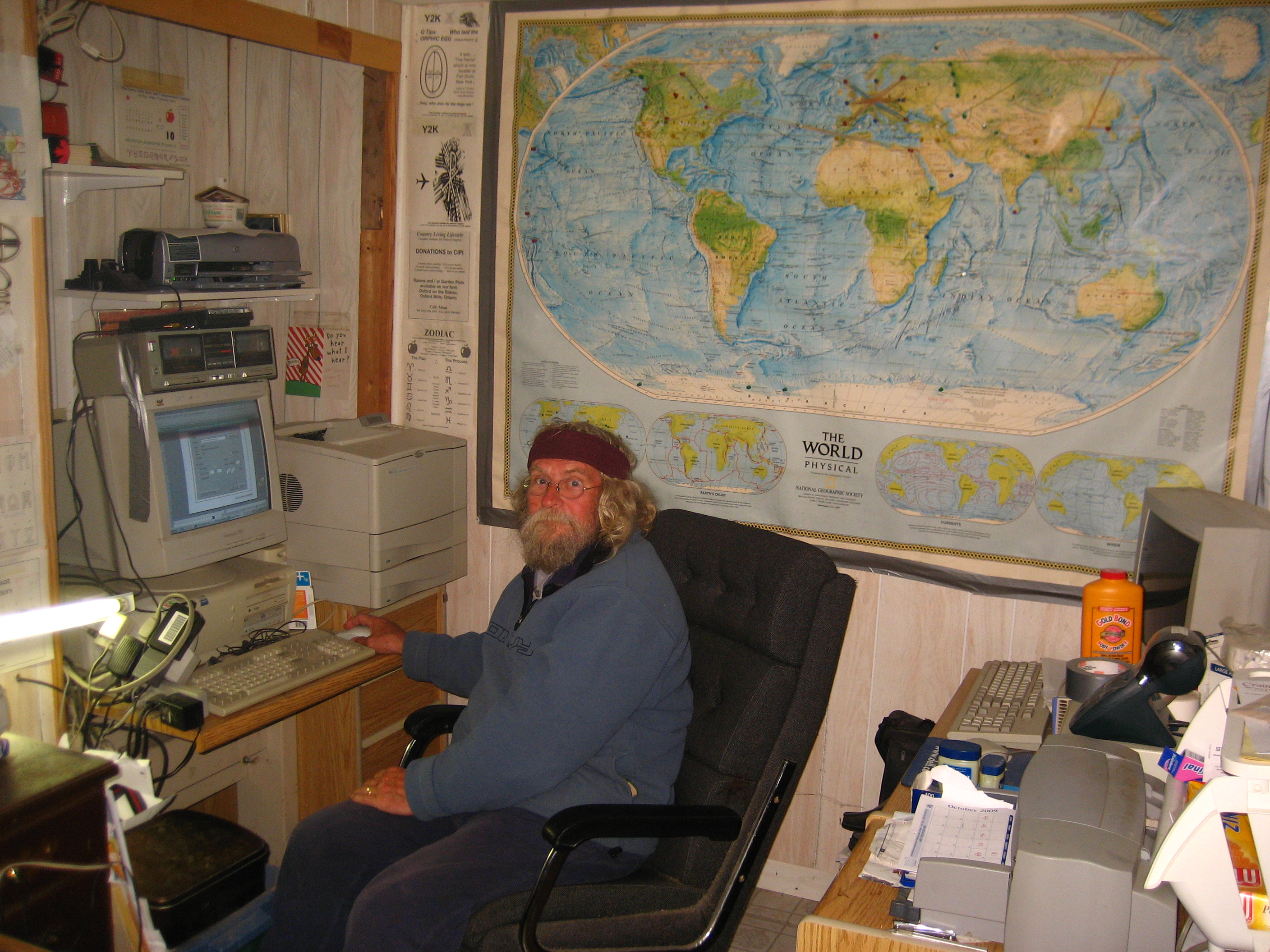 Glen Kealey at his desk, a world map marked with pins on the wall behind him
