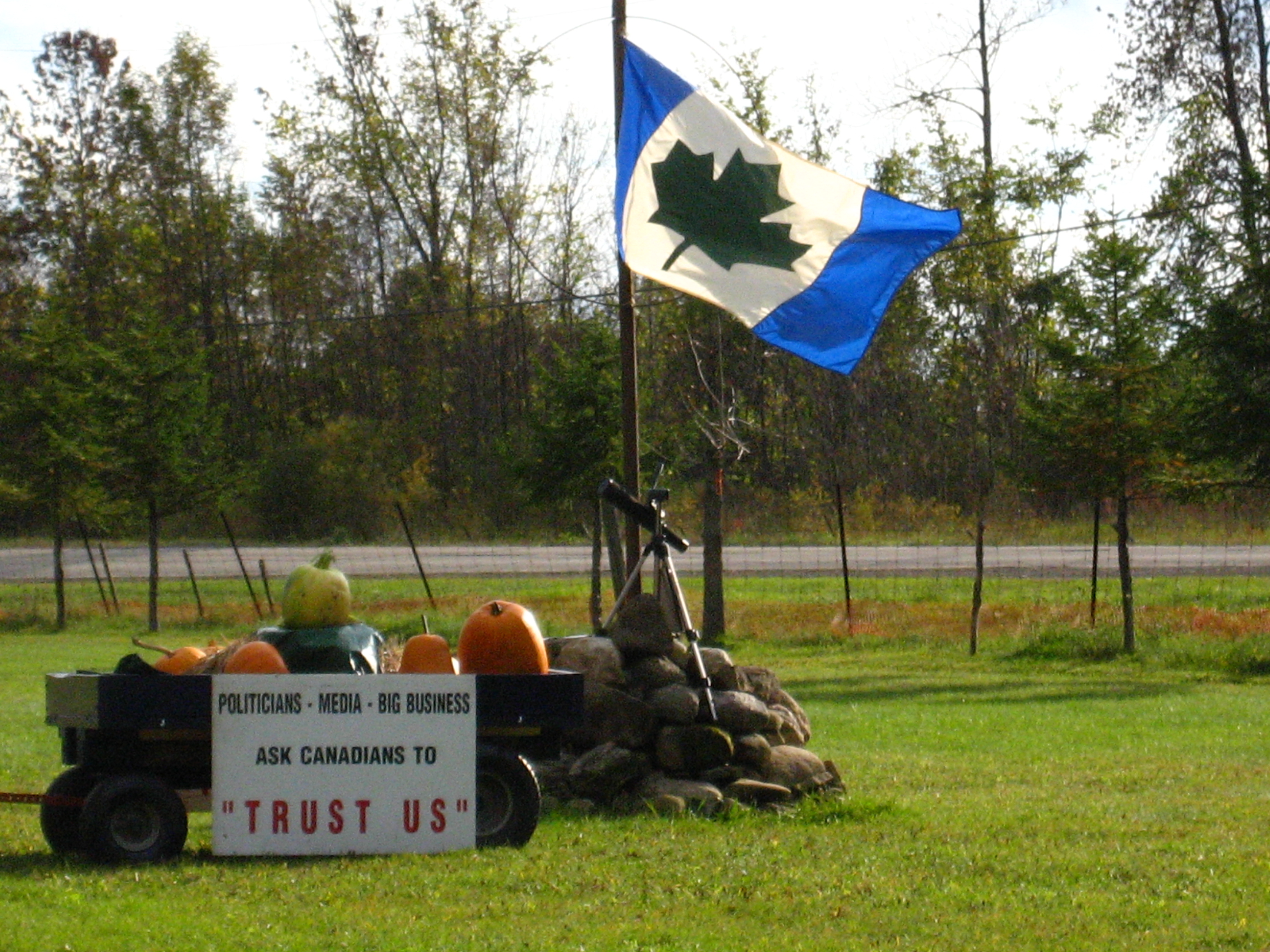 A flag and a wagon sign reading 'Politicians - Media - Big Business, ask Canadians to Trust Us' on Glen Kealey's farm